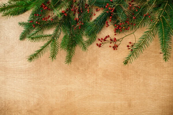 圣诞树的枝条和红色的浆果铺在粗糙的木头上 平整地躺着 季节的问候卡上有文字的空格 圣诞快乐及节日快乐 — 图库照片