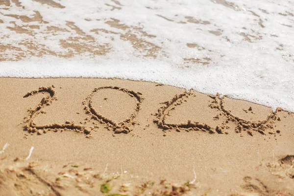 Good bye 2020 ! Wave with foam covering 2020 sign on sandy beach, leaving awful year 2020 behind. Welcoming new year 2021!