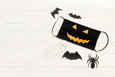 Cadılar Bayramı 2020 güvenli bir kutlama. Şeytani yüz maskesi, dezenfeksiyon jeli şişesi, beyaz tahtada yarasa ve örümcek süslemeleri. Yaratıcı olun Koronavirüs salgınına karşı dikkatli olun