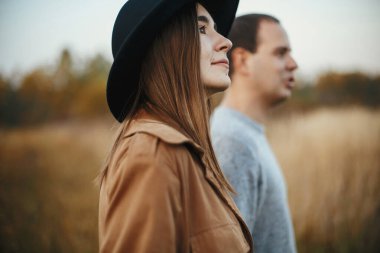 Günbatımında sonbahar tarlasında çimenlerin ve otların arasında yürüyen şık bir çift. Genç, şık bir kadın ve erkek portresi. Romantik otantik an