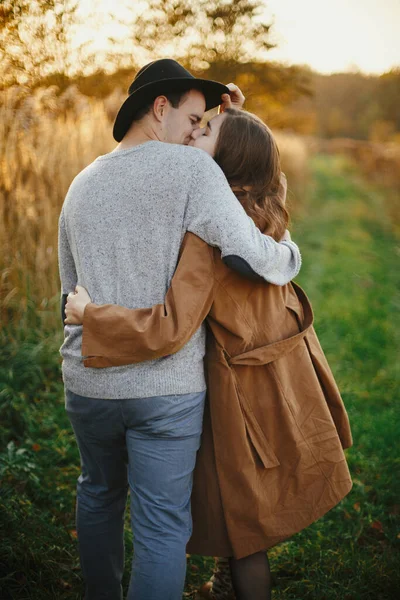 暖かい日没の光の中で秋の牧草地でキスを幸せなスタイリッシュなカップル ロマンチックな官能的な瞬間 若いですファッショナブルな女性と男を受け入れ秋のフィールド — ストック写真