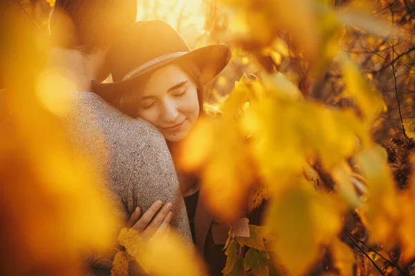 黄金の秋の葉の間に優しく抱きつくスタイリッシュな官能的なカップルは暖かい日没の光の中で 若いファッショナブルな女性は 秋の木に抱擁男を閉じると ロマンチックな瞬間 — ストック写真