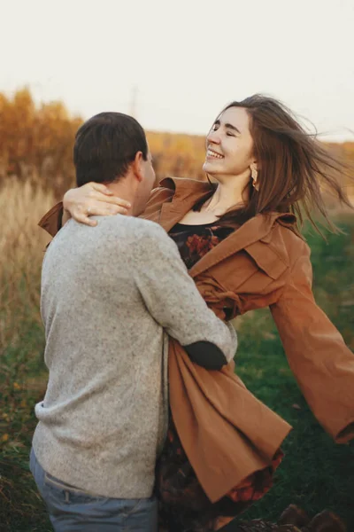 暖かい日没の光の中で秋の牧草地で踊る幸せなスタイリッシュなカップル ロマンチックな官能的な瞬間 若い感情的な女性と男の笑顔と秋のフィールドで旋回 — ストック写真