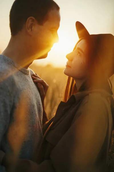 秋のフィールドで暖かい夕日の光に包まれたスタイリッシュな官能的なカップル 若いファッショナブルな女性と男性が優しく太陽の光を背景に抱擁 ロマンチックな本物の瞬間 — ストック写真