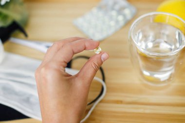 Ahşap masanın arka planında D vitamini, yüz maskesi, dezenfektan, termometre ve limon. Bağışıklık sistemini desteklemek, koronavirüs tedavisi. Sağlıklı kalın