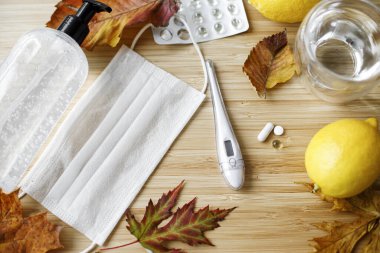 D vitamini, C vitamini ve çinko hapları maske, dezenfeksiyon jeli, limon, termometre ve dökülen yapraklarla ahşap masada. Sonbahar gribi ya da koronavirüs mevsiminde bağışıklık sisteminin desteklenmesi, konsept