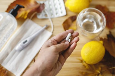 Sonbahar gribi mevsiminde veya koronavirüste bağışıklık sistemini güçlendirir. D vitamini, C vitamini ve çinko hapları arka plandaki tahta masanın üzerine düşmüş yapraklar, yüz maskesi, dezenfektan, limonlar.