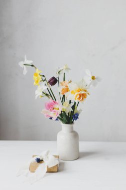Kırsal beyaz masa üzerinde kurdele ve bahar çiçekleri olan şık bir hediye kutusu. Mutlu kadınlar günü ve anneler günü. Güzel nergisler ve laleler. Nazik buket ve hediye. Metin için boşluk