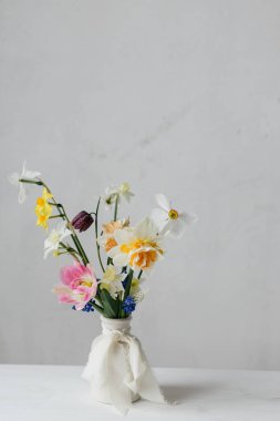 Kırsal beyaz masa üzerinde kurdeleli vazoda bahar çiçekleri. Mutlu kadınlar günü ve anneler günü. Güzel nergisler ve laleler. Nazik buket hayat. Metin için boşluk