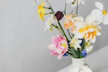 Kırsal beyaz masa üzerinde kurdeleli vazoda bahar çiçekleri. Mutlu kadınlar günü ve anneler günü. Güzel nergisler ve laleler. Nazik buket hayat. Metin için boşluk