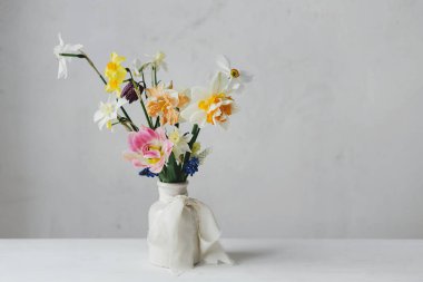 Kırsal beyaz masa üzerinde kurdeleli vazoda bahar çiçekleri. Mutlu kadınlar günü ve anneler günü. Güzel nergisler ve laleler. Nazik buket hayat. Metin için boşluk