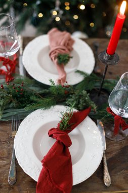 Aile yemeği için şık bir Noel sofrası. İçinde peçete, çatal bıçak takımı, cam, kurdele, yeşil köknar dalları, kırmızı böğürtlen ve mum olan şık bir tabak. Tatil zamanı.