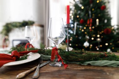Mutlu Noeller! Noel aile yemeği için şık bir masa. Modern tabak ve çatal bıçak, peçete, cam, yeşil ve kırmızı kurdele, köknar dalları ve kırsal masada mum.