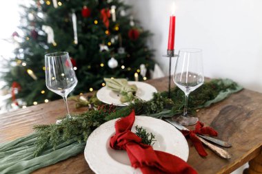 Aile yemeği için şık bir Noel sofrası. İçinde peçete, çatal bıçak takımı, cam, kurdele, yeşil köknar dalları, kırmızı böğürtlen ve mum olan şık bir tabak. Tatil zamanı.