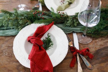 Aile yemeği için şık bir Noel sofrası. Peçete, çatal bıçak, cam, kurdele, yeşil köknar dalları, ahşap masa üzerindeki kırmızı böğürtlen manzaralı zarif bir tabak. Noel Tatil Zamanı