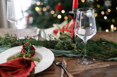 Mutlu Noeller! Noel aile yemeği için şık bir masa. Modern tabak ve çatal bıçak, peçete, cam, yeşil ve kırmızı kurdele, köknar dalları ve kırsal masada mum.