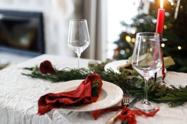 Modern tabaklar, kırmızı ve yeşil peçeteler, çatal bıçak takımı, cam, köknar dalları, kırmızı böğürtlen, keten masa örtüsünde mum. Mutlu Noeller ve mutlu tatiller!