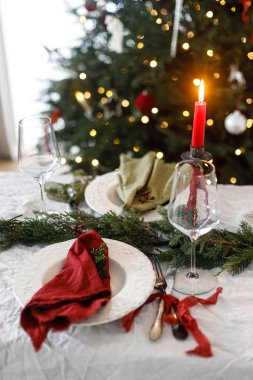 Mutlu Noeller! Noel aile yemeği için şık bir masa. Modern tabak ve çatal bıçak, peçete, cam, yeşil ve kırmızı kurdele, köknar dalları ve kırsal masada mum.