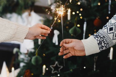 Mutlu yıllar! Süslü Noel ağacının ve şöminenin arka planında altın ışıklarla yanan maytaplar. Ellerinde parlayan havai fişekler, tatil kutlamaları