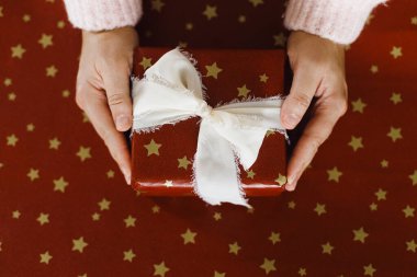 Mutlu Noeller ve mutlu tatiller! Kırmızı kağıdın üzerinde elleri şık bir noel hediyesi tutuyordu. Kırmızı kağıt ve ipek kurdeleli Xmas hediyesi. Tatil alışverişi konsepti