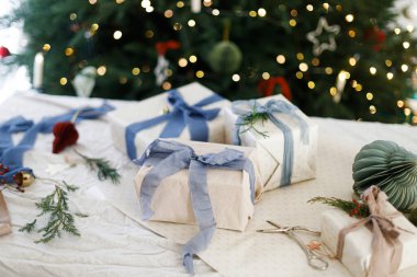 Mutlu Noeller ve mutlu tatiller! Mavi kurdeleler, yeşil dallar ve makaslarla süslenmiş şık Noel hediyeleri. Işıklı Noel ağacına karşı. Atmosfer zamanı