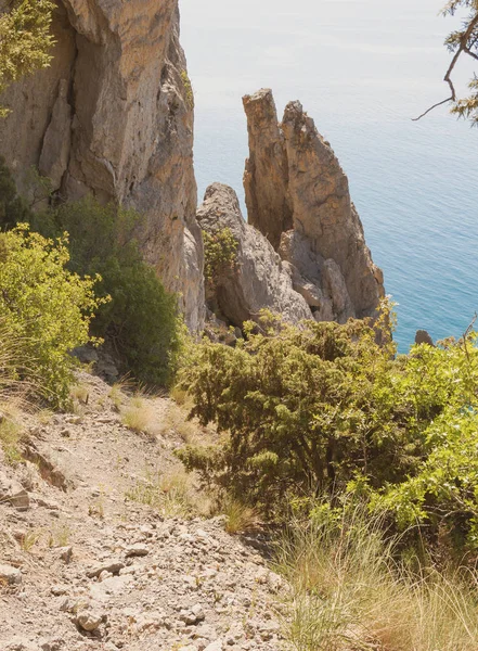 The mountain path goes down to the free-standing narrow rocks protruding from the water.