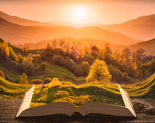 Girl hiker near the camping tent on a hill in a mountain valley on the pages of an open magical book. Majestic landscape. Nature and education concept.