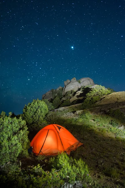 Illuminated camping travel tent in a mountains under the starry night sky.