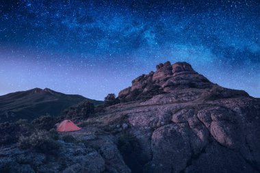 Bir gece gökyüzünde birçok yıldız ile bir dağ vadi kayalık tepenin kenarında kamp çadır. Açık ve seyahat kavramı.