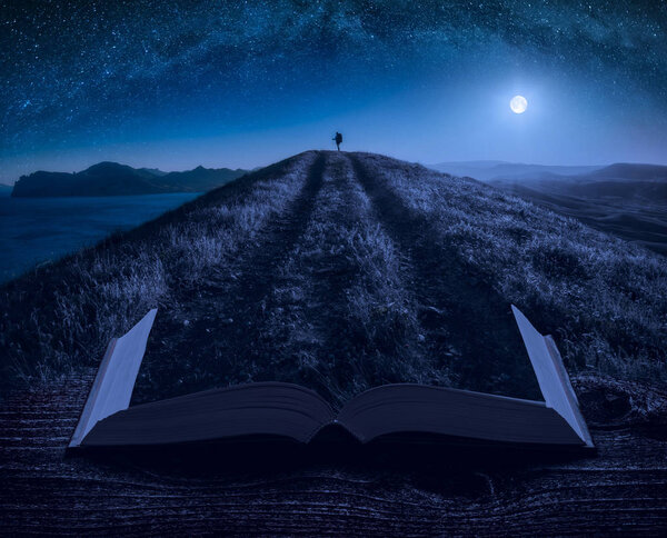 Girl hiker with backpack standing on a mountain top under the starry night sky on the pages of an open magical book. Majestic landscape. Travel concept.