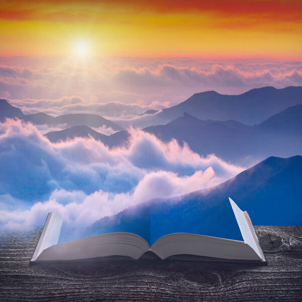 Sunrise above the foggy mountains valley on the pages of an open magical book. Majestic landscape. Nature and education concept.