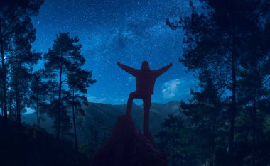 Kaldırdı elleriyle dağlar yukarıda yıldızlı gökyüzü karşı gece ormanın ortasında duran adam.