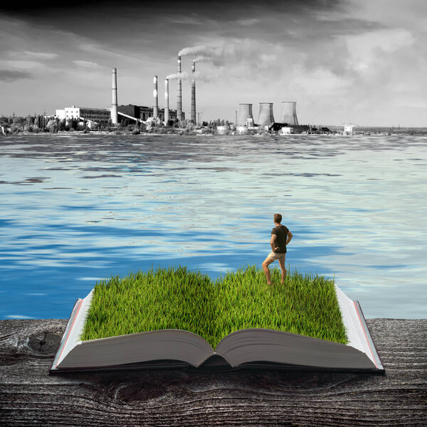 Man standing in a green grass on the pages of an open book against dark industrial background. Nature spring background. Ecology and education concept.