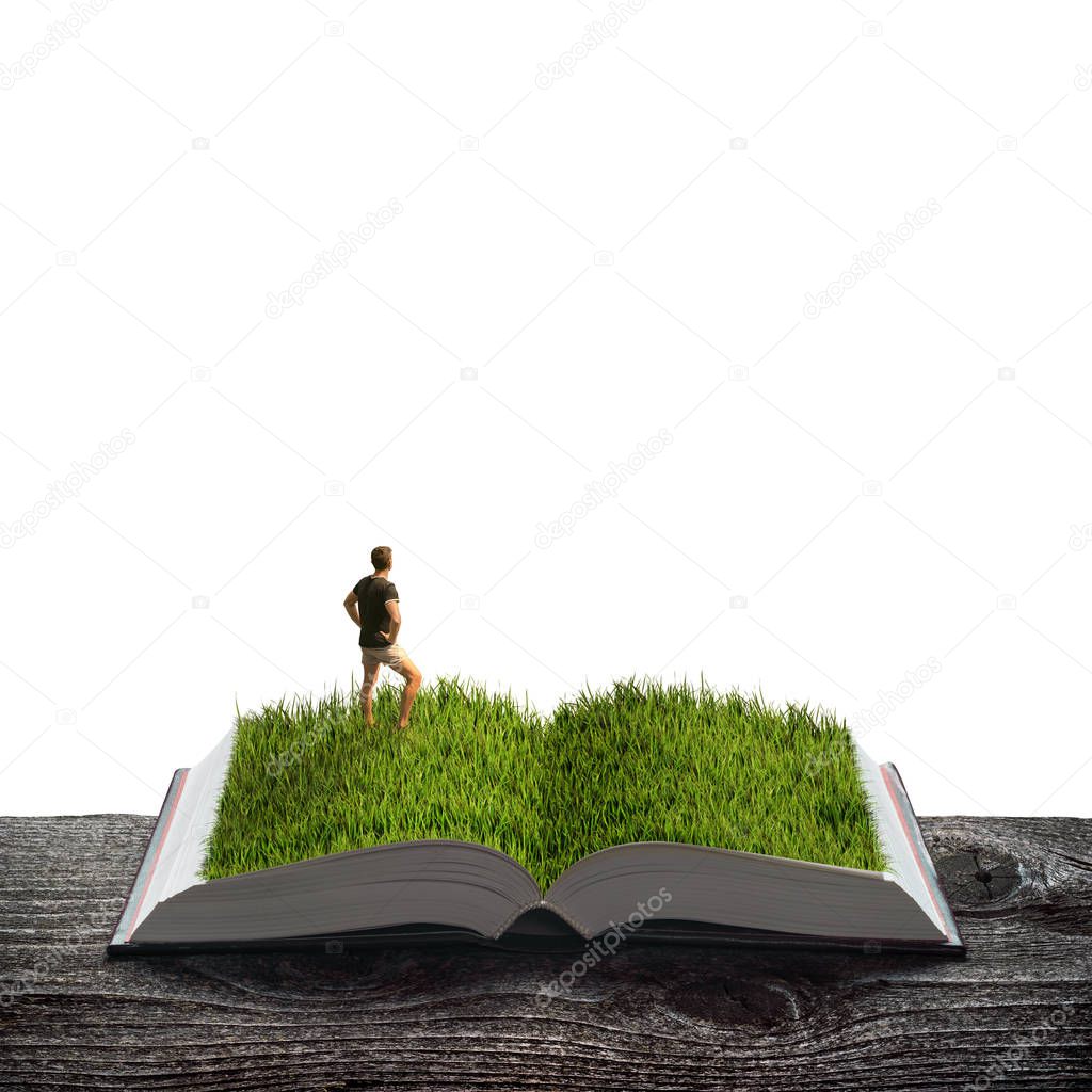 Young man standing in a green grass on the pages of an open magical book. Ecology and education concept.