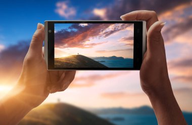 Akıllı telefon ekranında günbatımı ışıkta uzun yürüyüşe çıkan kimse