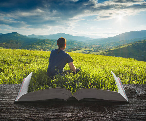 Man in a grass enjoy the valley on the pages of an open magical book. Majestic landscape. Travel and education concept.