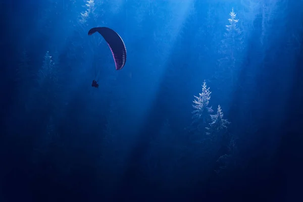Parachutist silhouette gliding over the foggy forest — Stock Photo, Image