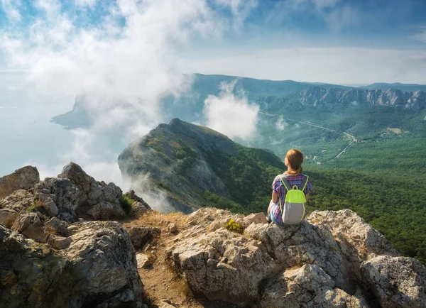 Lány túrázó a hátizsák ül a szikla szélén — Stock Fotó