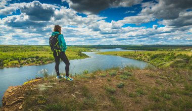 Sırt çantalı genç bir yürüyüşçü kız nehrin üzerindeki tepede duruyor. Seyahat kavramı.