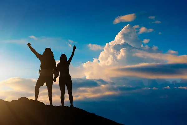 年轻的一对快乐的夫妇 背着背包在山顶上 在落日的天空中迎着蓬松的云彩 远足和探险概念 — 图库照片
