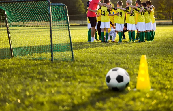 Futbol futbol eğitim genç erkekler için. Eğitim oturumu çim futbol sahası üzerinde. Futbol topu ve pilon koni ve futbol gol ön planda. Gençlik futbol takımı ayakta koç ile birlikte