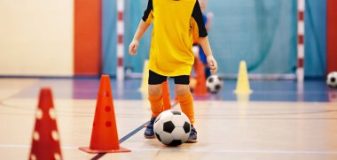 Futbol futsal eğitim çocuklar için. Futbol eğitim top sürme konik matkap. Kapalı futbol bir spor salonunda bir futbol topu ile genç oyuncu. Turuncu Tekdüzen oyuncunun. Spor arka plan