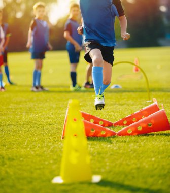 Genç sporcu çocuk futbol ekipmanları ile eğitim. Futbol hız eğitim. Genç futbolcu eğitim oturumunda çim futbol sahası üzerinde mavi spor giyim