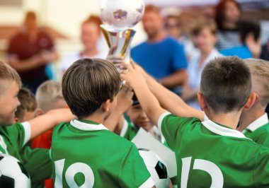 Çocuklar spor takım kazanmak için altın kupa yükselterek. Çocuklarda yeşil spor spor başarı kutluyor. Happy Kids zaferi kutlamak