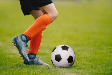 Bir futbol açık havada tekme bir genç adam. Genç futbolcu çim sahada eğitim. Bir spor giyim çocuk. Turuncu çorap ve futbol çizmeler giyen futbolcu. Futbol yatay arka plan