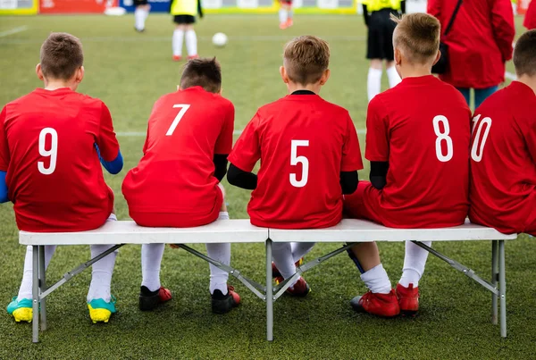 青年足球运动队坐在长椅上 作为替补运动员观看世界杯足球赛的年轻球员 男孩踢足球足球游戏在背景中 — 图库照片