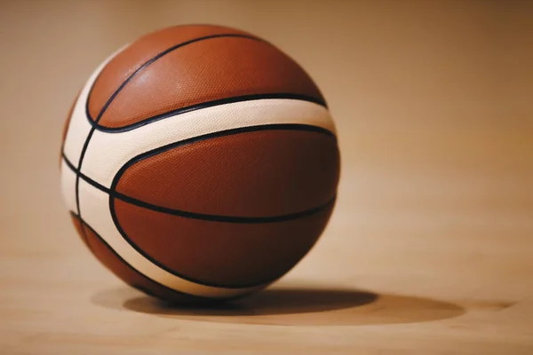 Basketball on Wooden Court Floor Close Up with Blurred Arena in Background. Orange Ball on a Hardwood Basketball Court