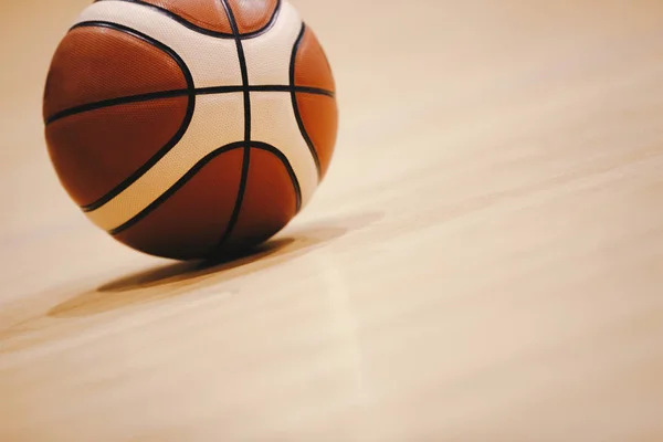 Basketball on Wooden Court Floor Close Up with Blurred Arena in Background. Orange Ball on a Hardwood Basketball Court