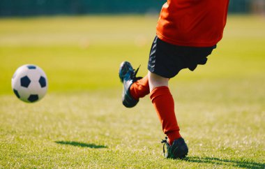 Genç futbolcu futbol sahada topu tekmeleme. Kırmızı spor Jersey, siyah şort, kırmızı futbol çorap ve siyah ayakkabısı giyen çocuk. Futbol tekme çim Stadı