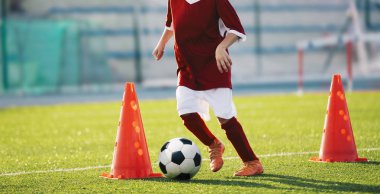 Gençlik futbol pratik matkaplar koniler ile. Futbol matkaplar: slalom matkap. Sahada eğitim genç futbol oyuncuları. Futbol slalom konik matkap. Kırmızı futbol jersey forması ile topu koni arasında çalışan çocuk